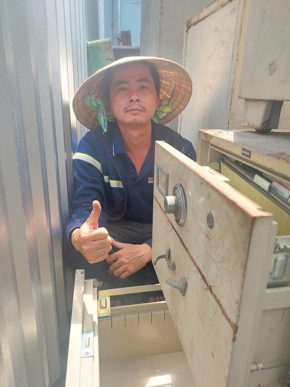 Thợ đội nón lá giơ ngón cái cạnh tủ két hồ sơ đã mở cửa