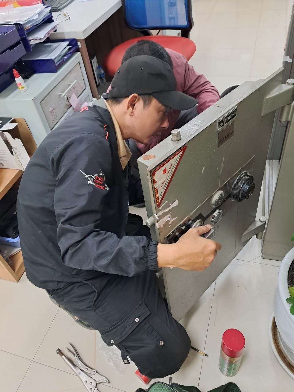 Kỹ thuật viên quỳ bên két sắt trong văn phòng, đồ nghề trải dưới sàn