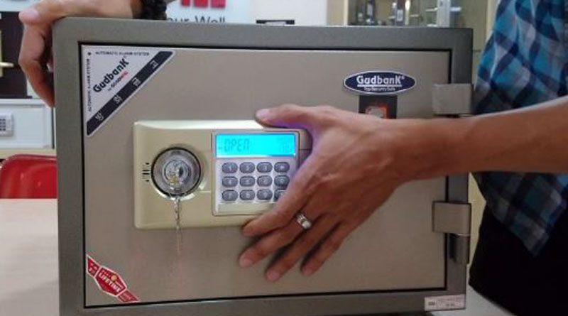 Két sắt điện tử Gudbank màu xám có ổ chìa, bàn phím và màn hình hiện chữ OPEN, tay người đặt trên bàn phím
