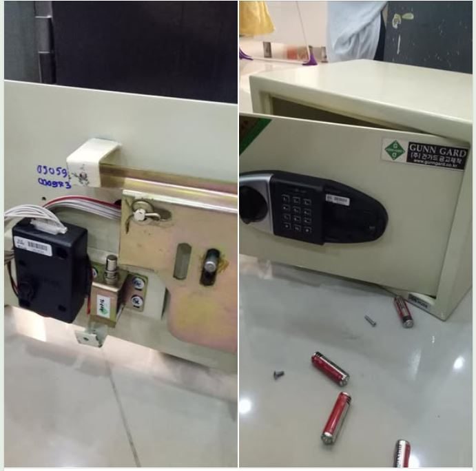 Mặt trong cánh két điện tử tháo nắp lộ hộp điều khiển, dây nối và chốt; bên cạnh là két mở cửa, pin rơi trên sàn