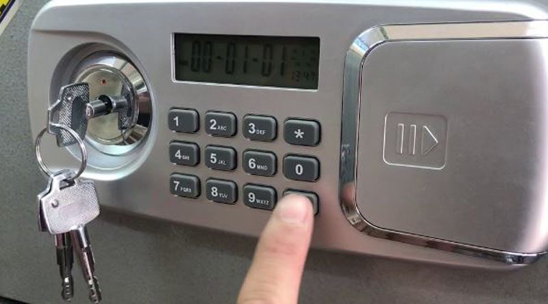 Ngón tay bấm bàn phím két điện tử màn hình LCD, ổ chìa bên trái đang cắm chìa
