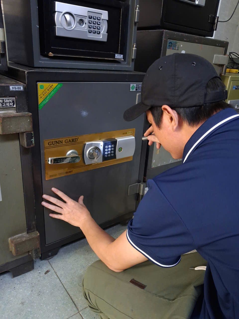 Thợ ngồi xổm đặt tay lên cánh két chống cháy Gunn Gard để kiểm tra khe cửa, phía trên có két nhỏ