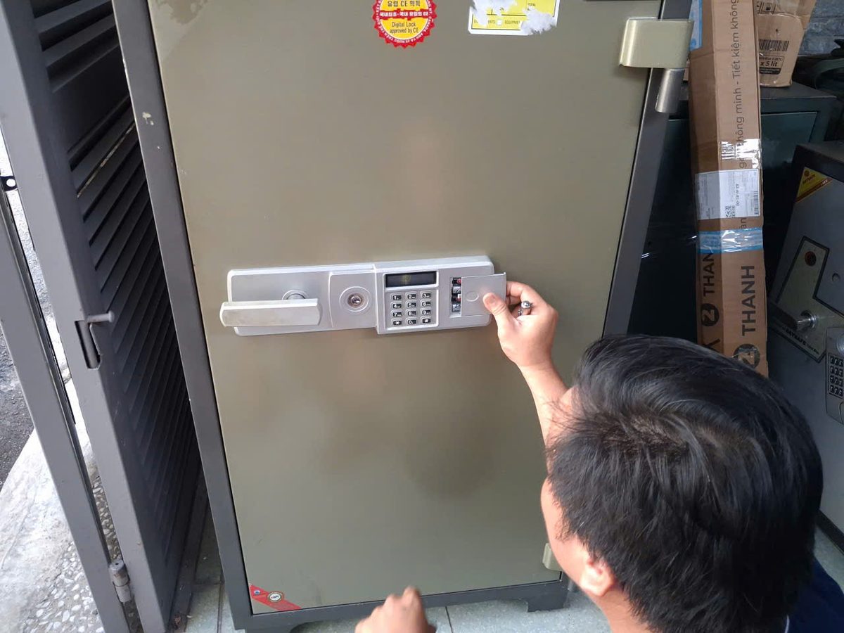 Thợ mở nắp hộp pin cạnh bàn phím trên két điện tử cỡ lớn đặt sát vách