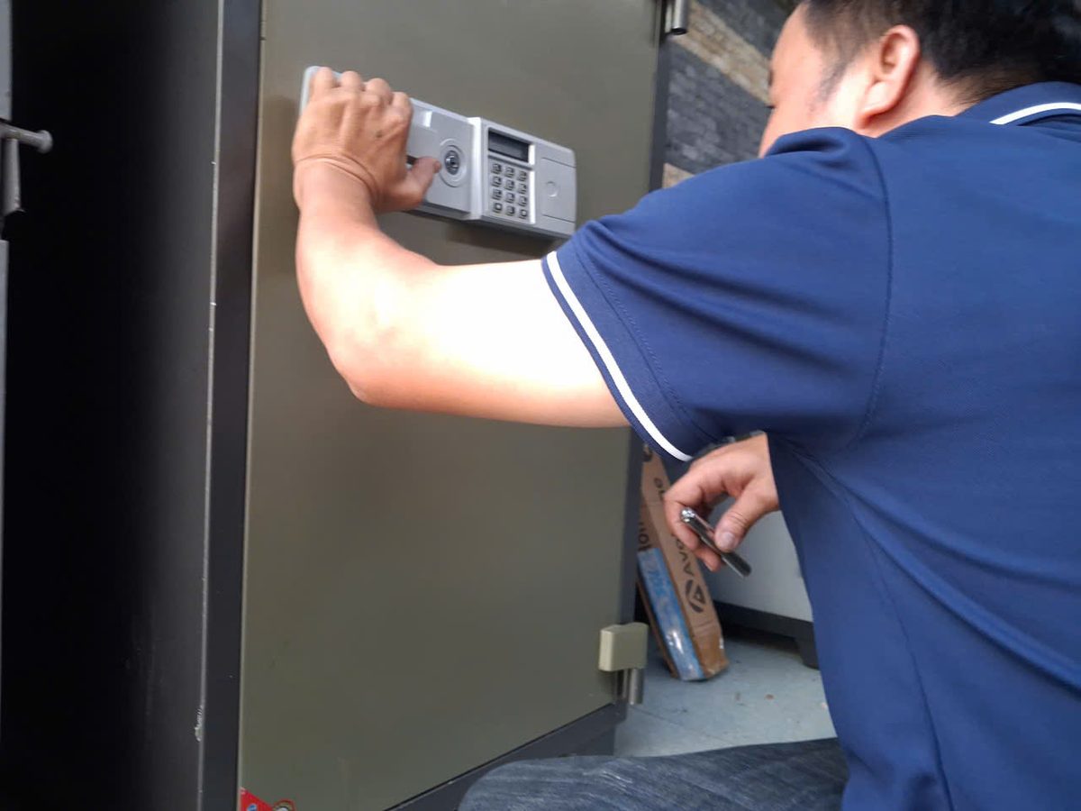Thợ một tay giữ cụm bàn phím két điện tử, tay kia cầm chìa đưa vào ổ phụ