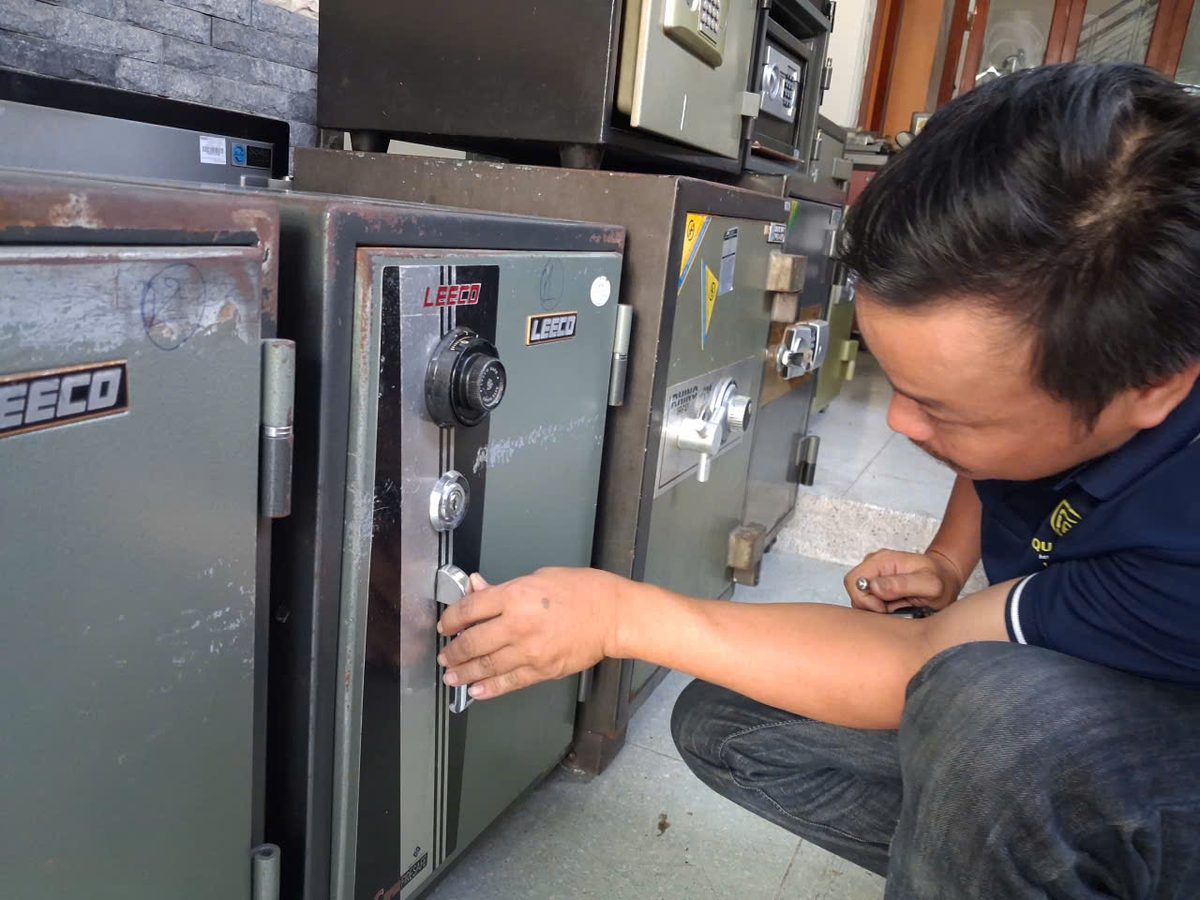 Thợ đội mũ cúi người nắm tay nắm mạ crôm của két Leeco để thử mở cửa