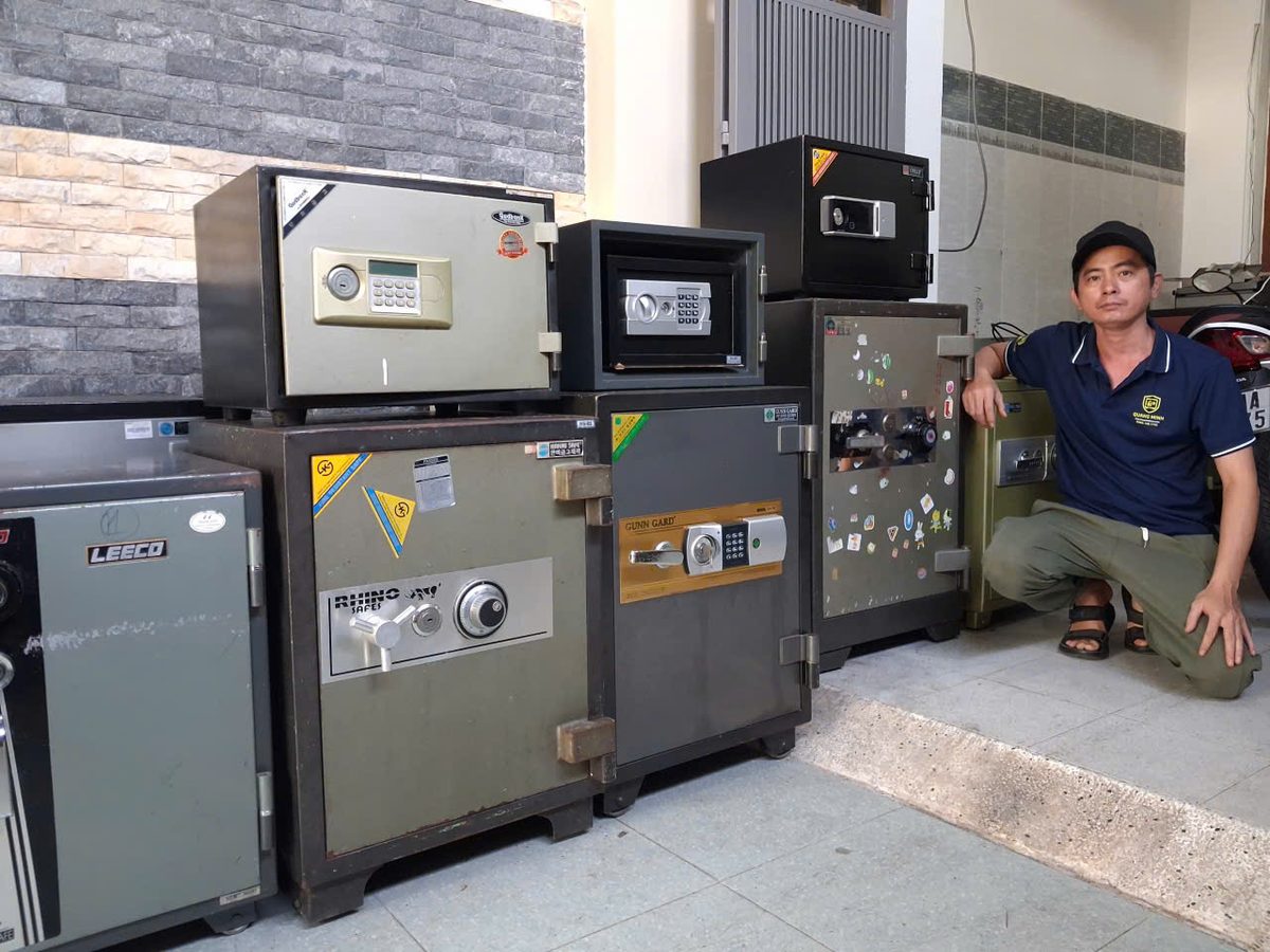 Thợ ngồi xổm bên dãy két sắt cơ và két điện tử chống cháy nhiều cỡ, có két màn hình đặt phía trên