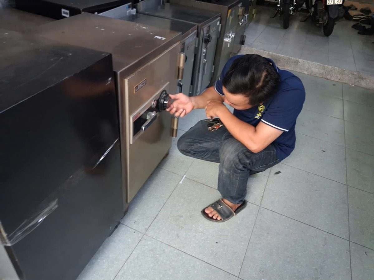 Thợ ngồi xổm trên nền gạch xoay núm số của két sắt cơ Leeco màu nâu đồng