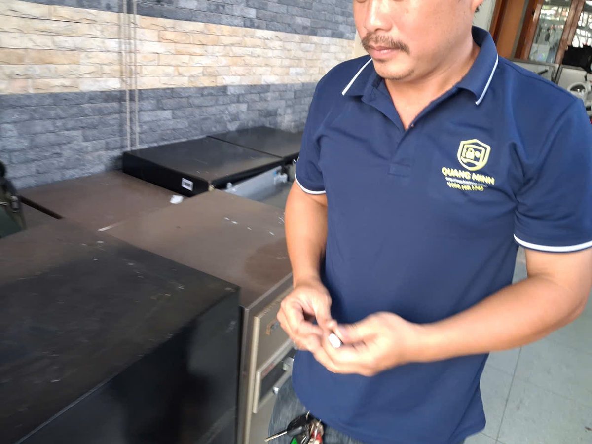 Thợ Quang Minh cầm chiếc chìa két nhỏ trên tay, đứng cạnh dãy két sắt cũ